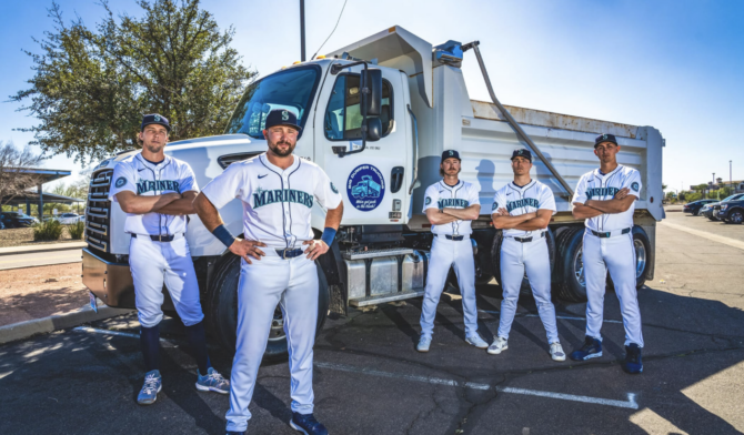 Four Mariners players stand in front of a dump truck.